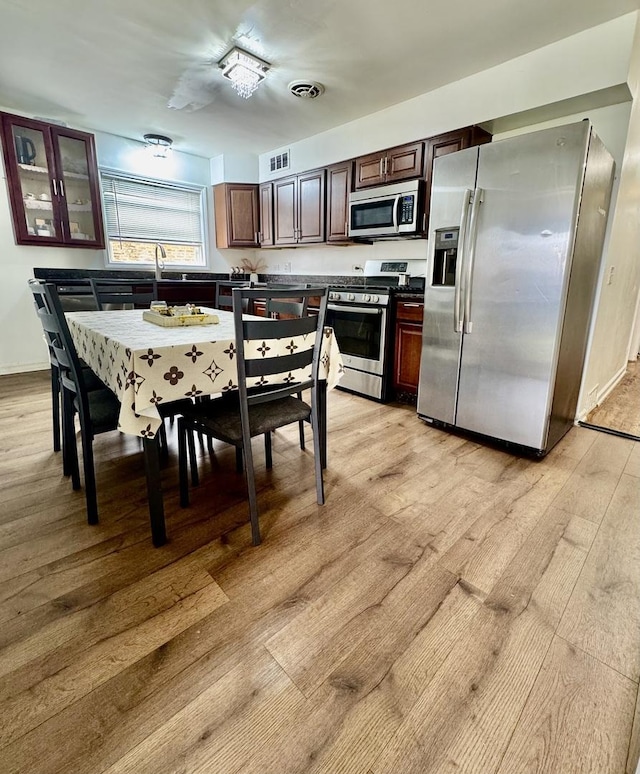 6531 N Hoyne Ave Unit 2S, Chicago, IL 60645 - kitchen featuring stainless steel appliances, light wood finished floors, dark brown cabinetry, and glass insert cabinets
