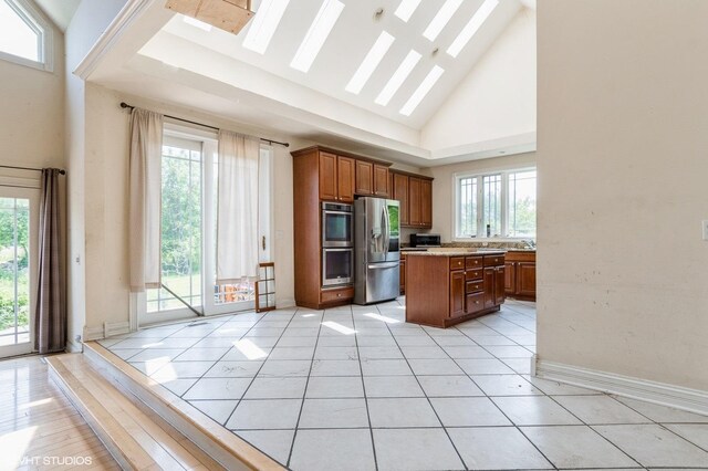 4722 Douglas Rd, Oswego, IL 60543 - kitchen with stainless steel appliances, high vaulted ceiling, brown cabinetry, a kitchen island, and light countertops