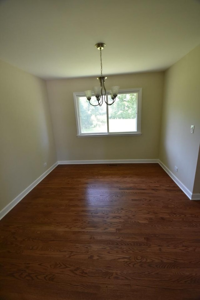 spare room with a chandelier and dark wood-type flooring