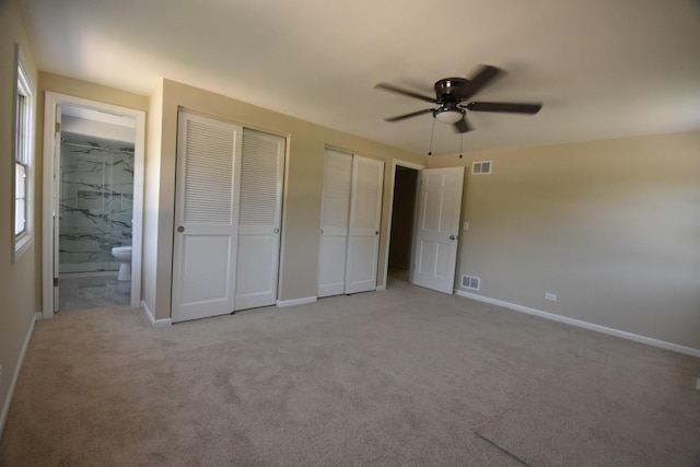 unfurnished bedroom featuring two closets, light carpet, ensuite bath, and a ceiling fan