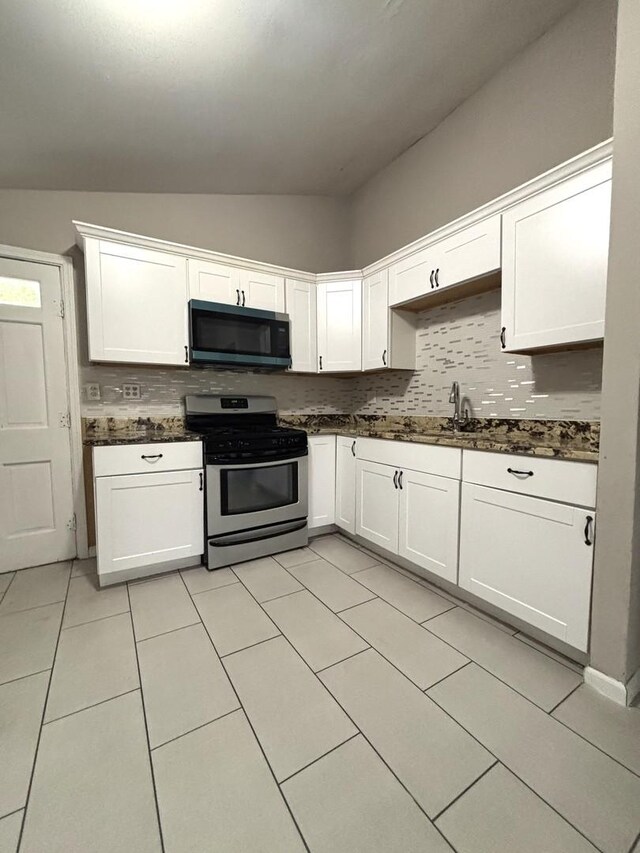 1403 Kings Rd, Carpentersville, IL 60110 - kitchen featuring black microwave, stainless steel range with gas stovetop, lofted ceiling, tasteful backsplash, and white cabinets