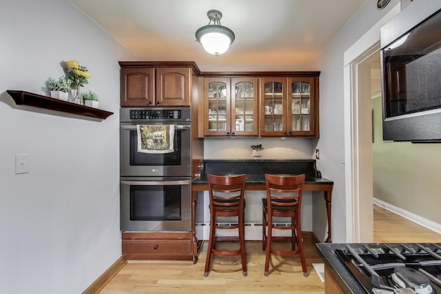 1350 Saint Johns Ave, Highland Park, IL 60035 - kitchen featuring stainless steel appliances, dark countertops, light wood-style flooring, a kitchen breakfast bar, and glass insert cabinets