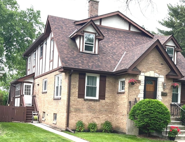 9907 Kedvale Ave, Skokie, IL 60076 - tudor-style house featuring roof with shingles, a chimney, a front lawn, and brick siding