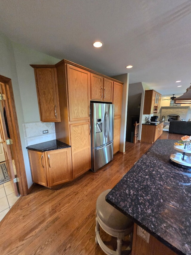 10880 Swallow Tail Ln, Frankfort, IL 60423 - kitchen with stainless steel fridge, brown cabinetry, dark stone countertops, wood finished floors, and a fireplace