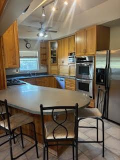 785 Alice St, Chicago Heights, IL 60411 - kitchen with stainless steel appliances, a peninsula, a breakfast bar, ceiling fan, and brown cabinets