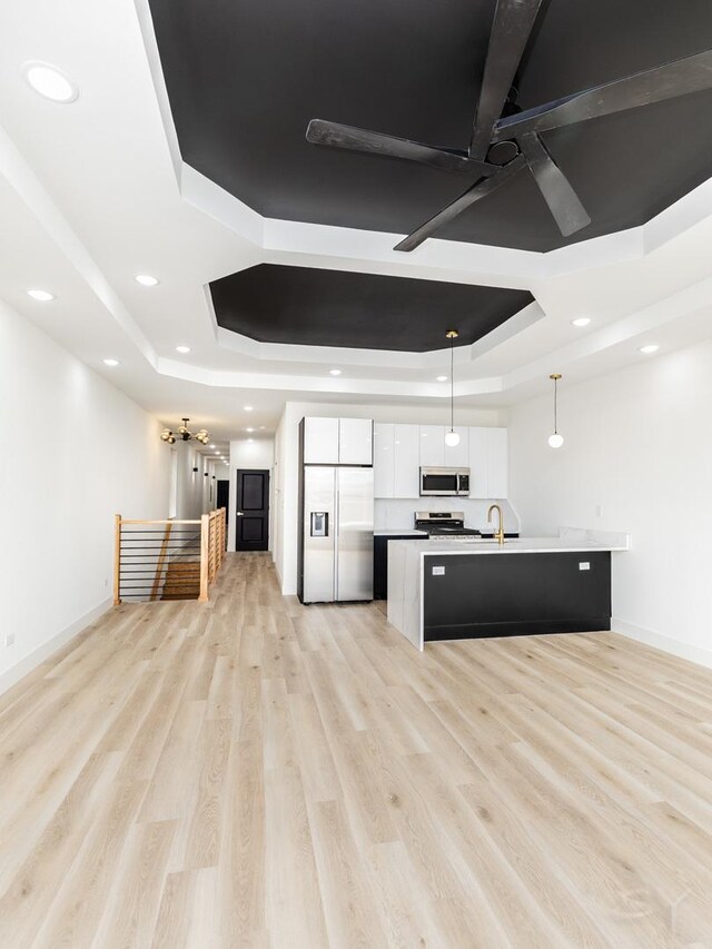5534 S Michigan Ave, Chicago, IL 60637 - kitchen featuring stainless steel appliances, a tray ceiling, white cabinets, light wood-type flooring, and an island with sink