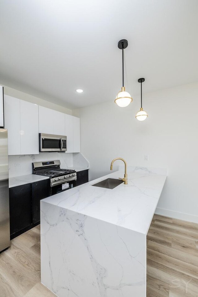 5534 S Michigan Ave, Chicago, IL 60637 - kitchen featuring stainless steel appliances, a sink, a peninsula, decorative light fixtures, and white cabinetry
