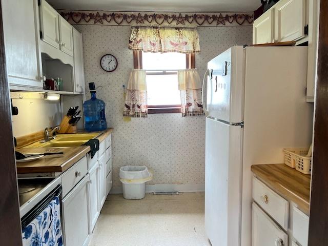 520 W American St, Freeport, IL 61032 - kitchen with wallpapered walls, freestanding refrigerator, a sink, white cabinets, and stainless steel electric stove