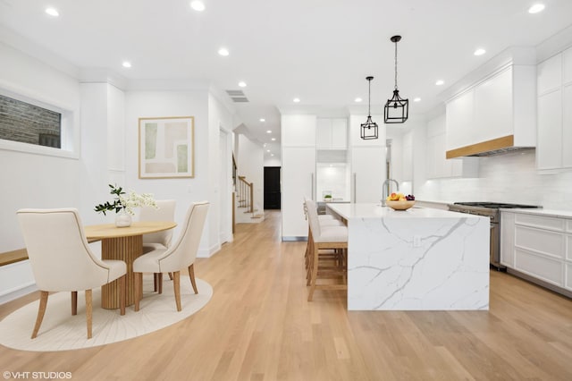 4242 N Winchester Ave, Chicago, IL 60613 - kitchen featuring stainless steel range, an island with sink, light wood-type flooring, recessed lighting, and white cabinets