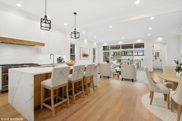 4242 N Winchester Ave, Chicago, IL 60613 - kitchen featuring tasteful backsplash, a sink, high end stainless steel range oven, an island with sink, and light wood finished floors