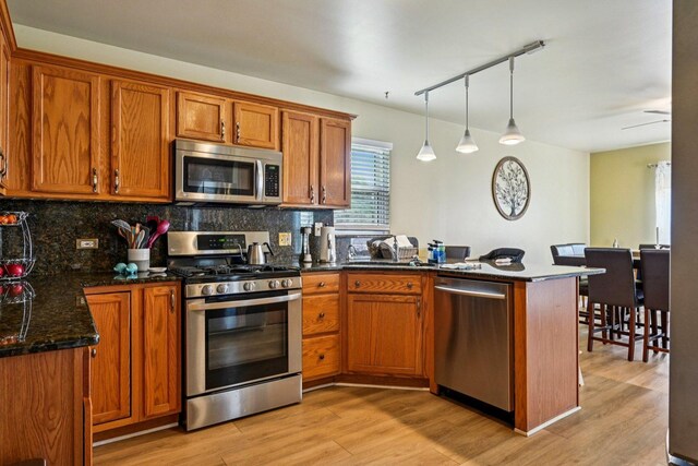 1043 San Mateo Dr, Romeoville, IL 60446 - kitchen featuring appliances with stainless steel finishes, a peninsula, brown cabinets, decorative backsplash, and track lighting