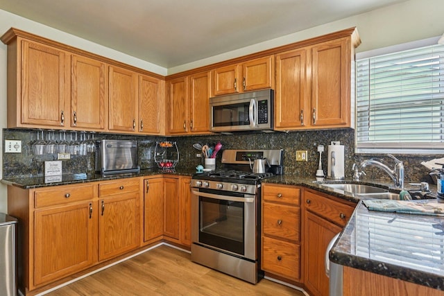 1043 San Mateo Dr, Romeoville, IL 60446 - kitchen featuring stainless steel appliances, a sink, brown cabinets, light wood-style floors, and dark stone counters