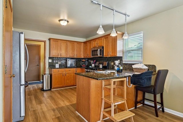 1043 San Mateo Dr, Romeoville, IL 60446 - kitchen with appliances with stainless steel finishes, a peninsula, rail lighting, wood finished floors, and decorative backsplash