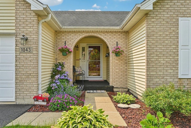 1043 San Mateo Dr, Romeoville, IL 60446 - view of exterior entry with brick siding, roof with shingles, a garage, and covered porch