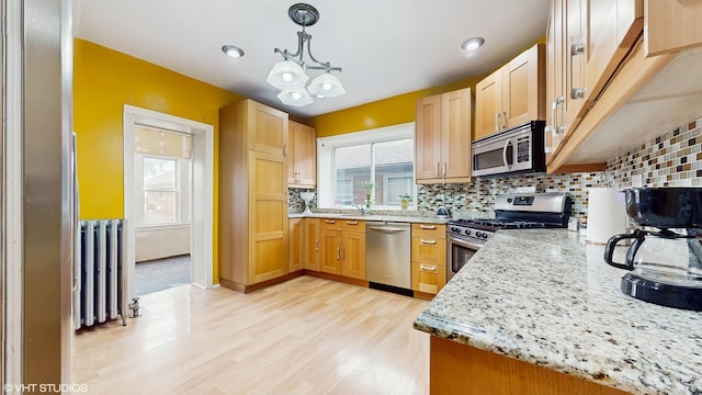 4608 W Altgeld St, Chicago, IL 60639 - kitchen with appliances with stainless steel finishes, radiator, light wood finished floors, backsplash, and light stone counters