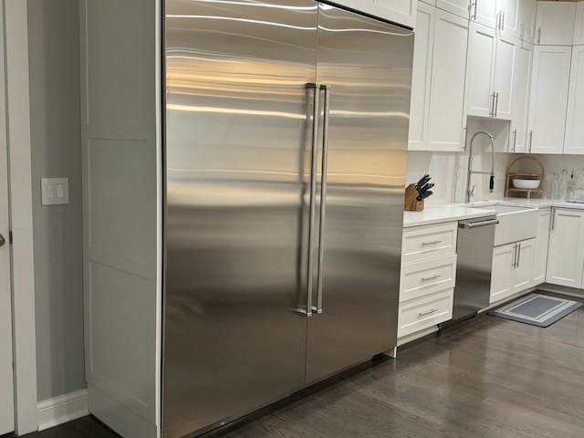 kitchen featuring appliances with stainless steel finishes, dark wood-style flooring, light countertops, white cabinets, and a sink