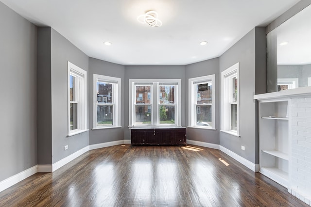 spare room with wood finished floors, baseboards, built in shelves, radiator, and recessed lighting