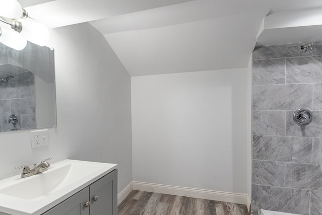 bathroom with vanity, a tile shower, wood finished floors, lofted ceiling, and baseboards