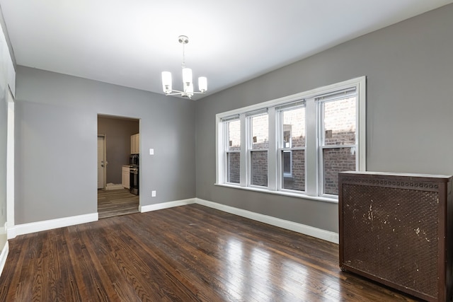 empty room with a chandelier, dark wood finished floors, and baseboards