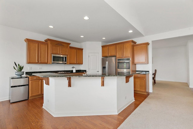 23521 N Sanctuary Club Dr, Kildeer, IL 60047 - kitchen featuring stainless steel appliances, brown cabinets, a kitchen bar, recessed lighting, and dark stone countertops