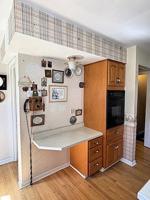 5N265 Neva Ter, Itasca, IL 60143 - kitchen featuring black oven, wallpapered walls, light wood-type flooring, brown cabinets, and light countertops