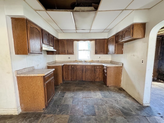 7514 S Rhodes Ave, Chicago, IL 60619 - kitchen with under cabinet range hood, stone tile floors, arched walkways, a sink, and decorative backsplash