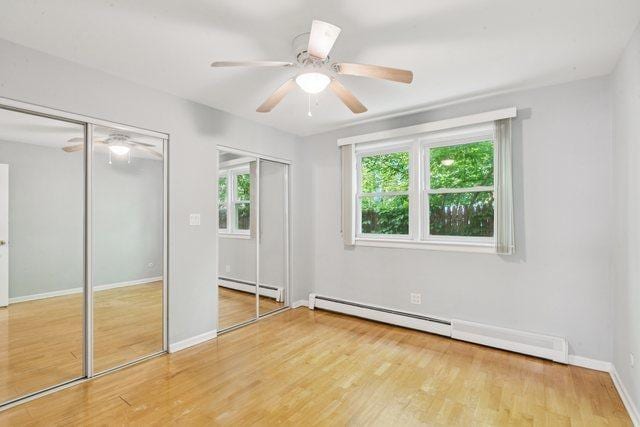 1819 W Touhy Ave Unit 2, Chicago, IL 60626 - unfurnished bedroom with baseboard heating, two closets, wood finished floors, and baseboards
