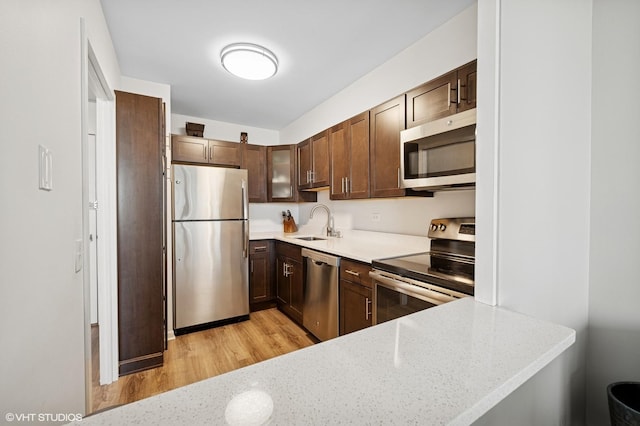 1560 N Sandburg Ter Unit 1605J, Chicago, IL 60610 - kitchen featuring stainless steel appliances, a sink, light wood finished floors, dark brown cabinets, and light stone counters