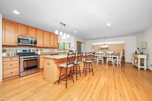 22314 Jeanette Ct, Frankfort, IL 60423 - kitchen featuring appliances with stainless steel finishes, light wood finished floors, a chandelier, a breakfast bar, and a center island