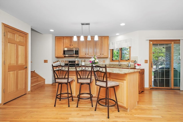 22314 Jeanette Ct, Frankfort, IL 60423 - kitchen featuring appliances with stainless steel finishes, light wood-style floors, a kitchen bar, a kitchen island, and recessed lighting