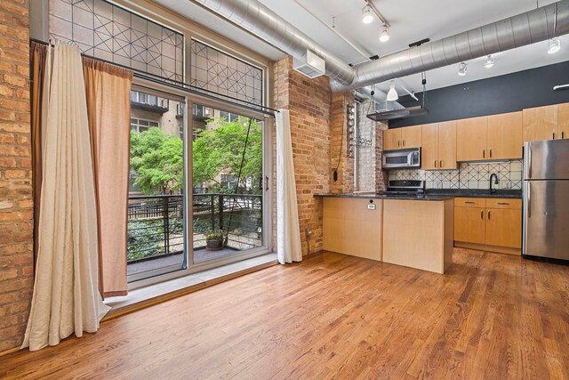 420 S Clinton St Unit 102A, Chicago, IL 60607 - kitchen with appliances with stainless steel finishes, brick wall, dark countertops, wood finished floors, and light brown cabinetry