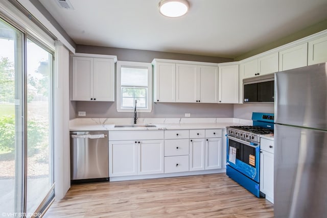 kitchen featuring appliances with stainless steel finishes, a sink, white cabinetry, light countertops, and light wood-style floors