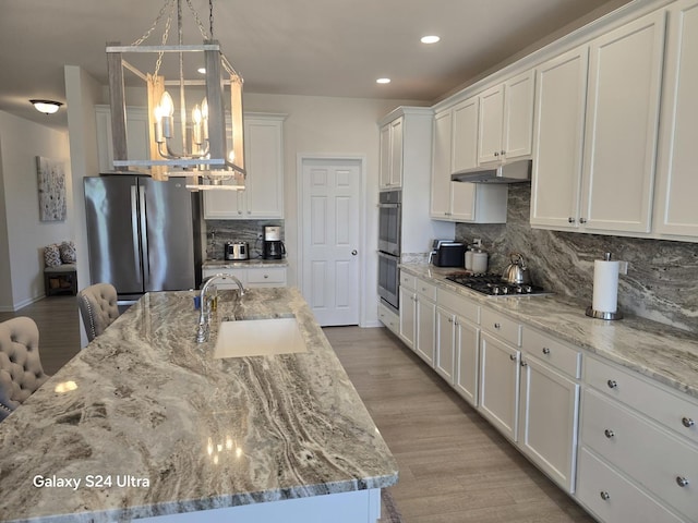 12305 S Prairie Ridge Ln, Plainfield, IL 60585 - kitchen featuring appliances with stainless steel finishes, under cabinet range hood, a chandelier, tasteful backsplash, and white cabinetry