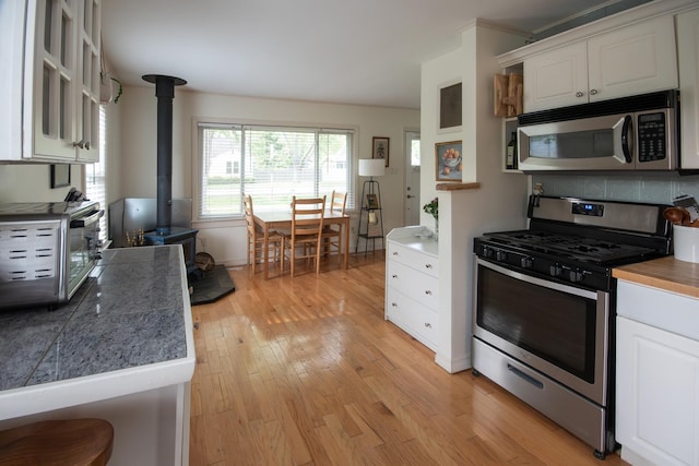 307 Highland Rd, Grayslake, IL 60030 - kitchen featuring stainless steel appliances, a wood stove, white cabinetry, light wood-style floors, and tile countertops