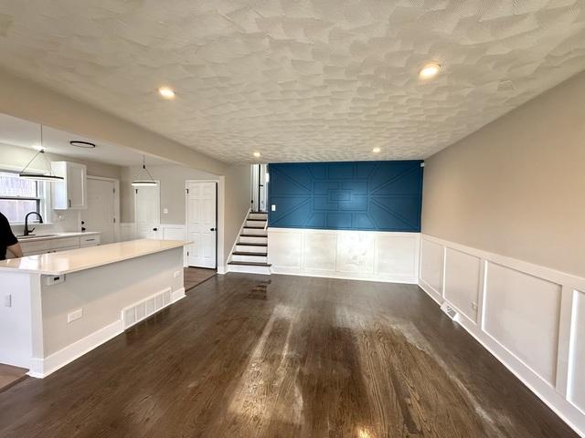 14409 Kimbark Ave, Dolton, IL 60419 - unfurnished living room with a sink, dark wood-style flooring, stairs, a decorative wall, and wainscoting