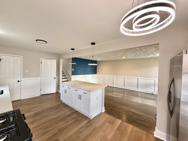 14409 Kimbark Ave, Dolton, IL 60419 - kitchen featuring freestanding refrigerator, wood finished floors, white cabinetry, wainscoting, and a decorative wall