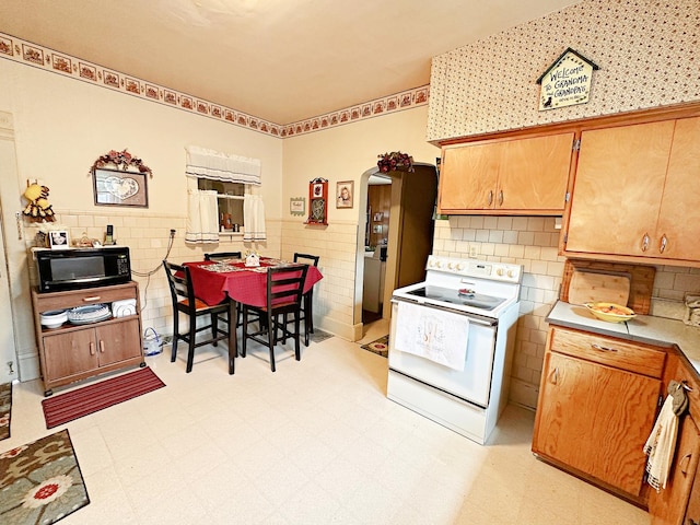 117 W 9th St, Streator, IL 61364 - kitchen with white electric range oven, tile walls, light flooring, arched walkways, and black microwave