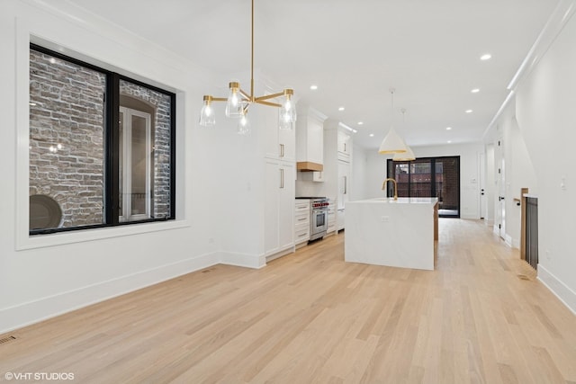 2118 N Sheffield Ave Unit 1, Chicago, IL 60614 - kitchen with stainless steel range, white cabinets, a center island with sink, light wood-style floors, and decorative light fixtures