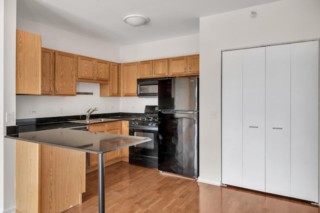 125 S Jefferson St Unit 710, Chicago, IL 60661 - kitchen featuring black appliances, a sink, dark countertops, light wood-style flooring, and a peninsula