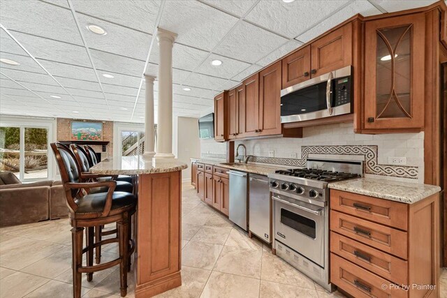 11 Moate Ln, Barrington Hills, IL 60010 - kitchen with appliances with stainless steel finishes, ornate columns, brown cabinets, glass insert cabinets, and recessed lighting