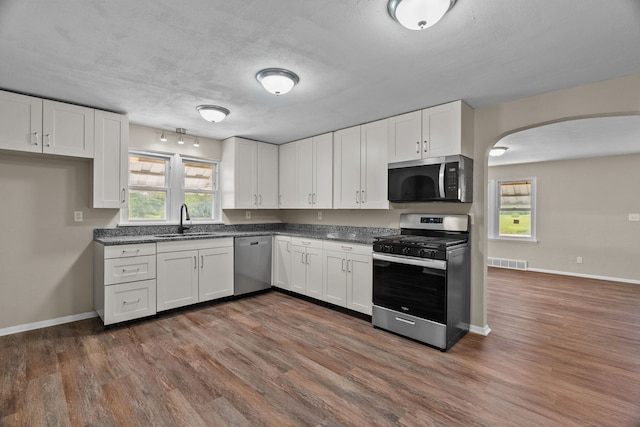 7832 Main St, Walsh, IL 62297 - kitchen featuring appliances with stainless steel finishes, a sink, dark countertops, arched walkways, and white cabinets