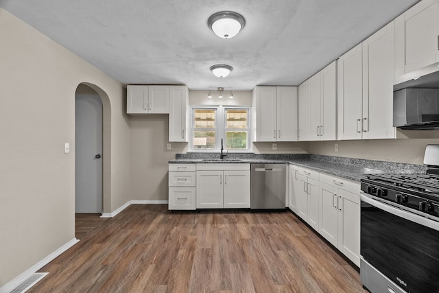 7832 Main St, Walsh, IL 62297 - kitchen featuring stainless steel appliances, a sink, dark wood-style floors, arched walkways, and white cabinetry