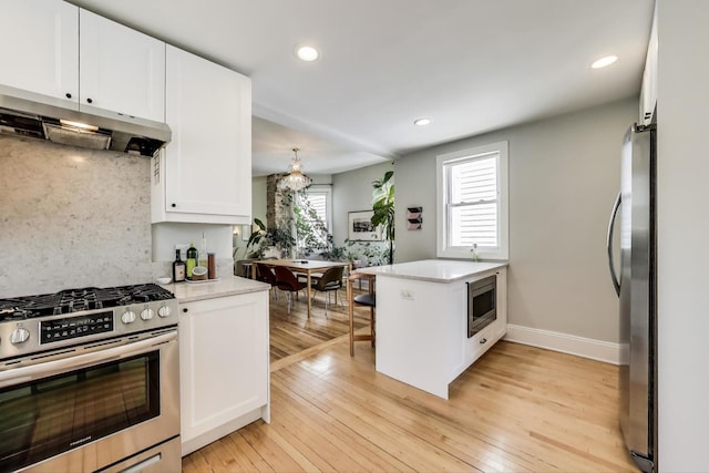 3719 W Shakespeare Ave, Chicago, IL 60647 - kitchen featuring stainless steel appliances, under cabinet range hood, a peninsula, white cabinetry, and light wood-style flooring