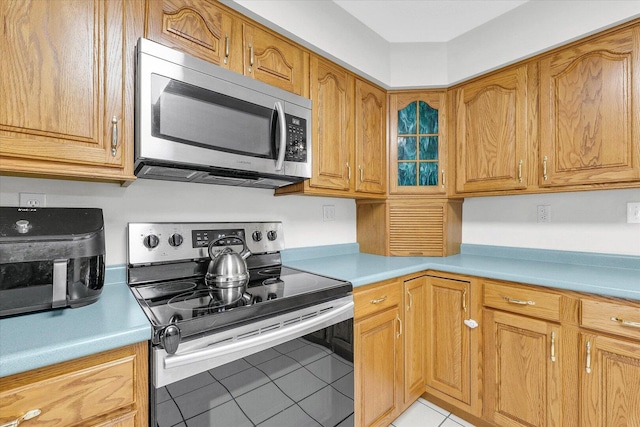 1803 Galena St, Urbana, IL 61802 - kitchen featuring stainless steel appliances, light tile patterned floors, light countertops, brown cabinets, and glass insert cabinets