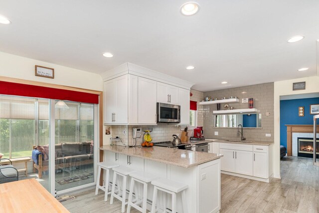 2715 Lahinch Dr, Aurora, IL 60503 - kitchen with appliances with stainless steel finishes, light stone countertops, a glass covered fireplace, white cabinets, and decorative backsplash