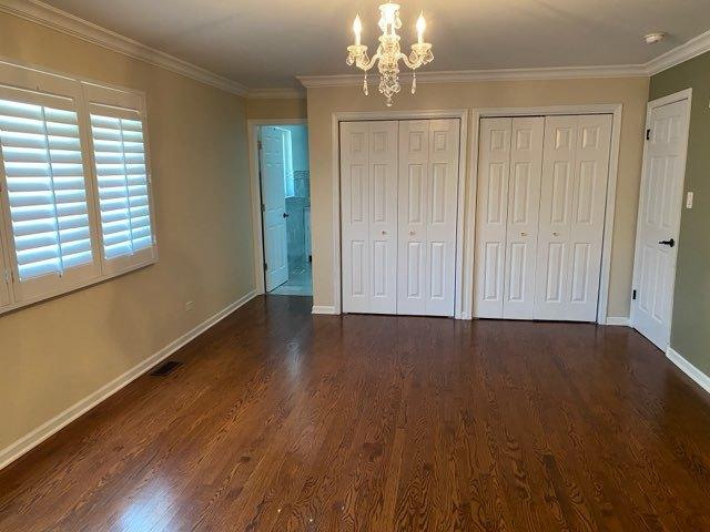 473 S Edgewood Ave, Wood Dale, IL 60191 - unfurnished bedroom featuring a chandelier, two closets, dark wood finished floors, baseboards, and crown molding