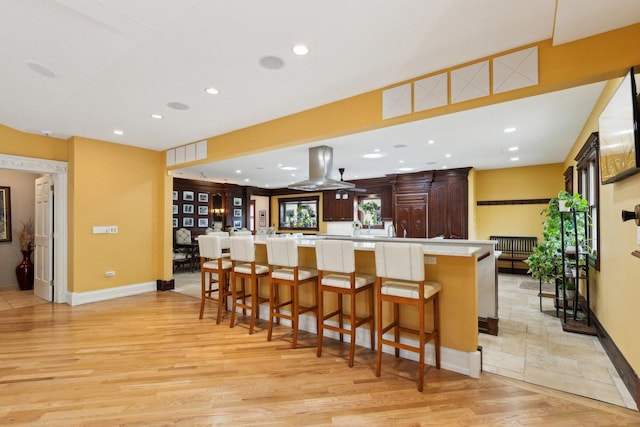 1424 Glencoe Ave, Highland Park, IL 60035 - kitchen featuring light wood-style floors, light countertops, island exhaust hood, a kitchen breakfast bar, and dark brown cabinets
