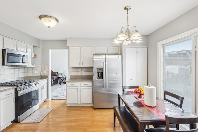 4801 Bordeaux Dr, Lake In The Hills, IL 60156 - kitchen with stainless steel appliances, light wood-style floors, backsplash, a chandelier, and white cabinetry
