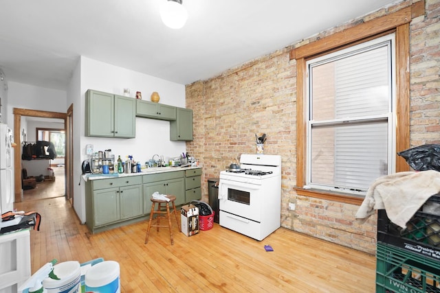 1518 N Kedzie Ave, Chicago, IL 60651 - kitchen featuring green cabinetry, white gas range, brick wall, light wood-style flooring, and a sink