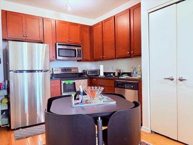 kitchen with appliances with stainless steel finishes, light wood-type flooring, dark countertops, and brown cabinets